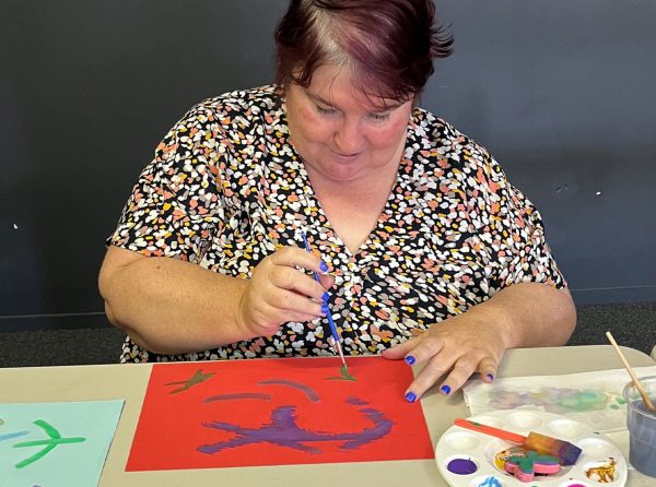 Woman painting artwork at a table with colourful paints and craft supplies during a creative activity session.